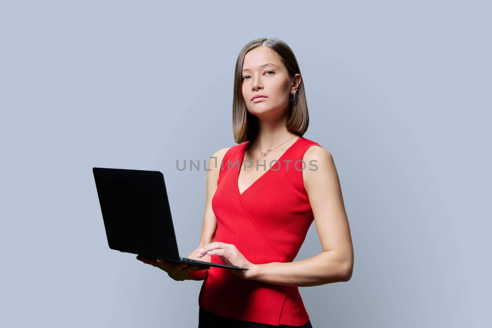 Serious young business woman with laptop on grey studio background. Successful confident caucasian female looking at camera. Business, work, job, study, education, e-learning, technology concept