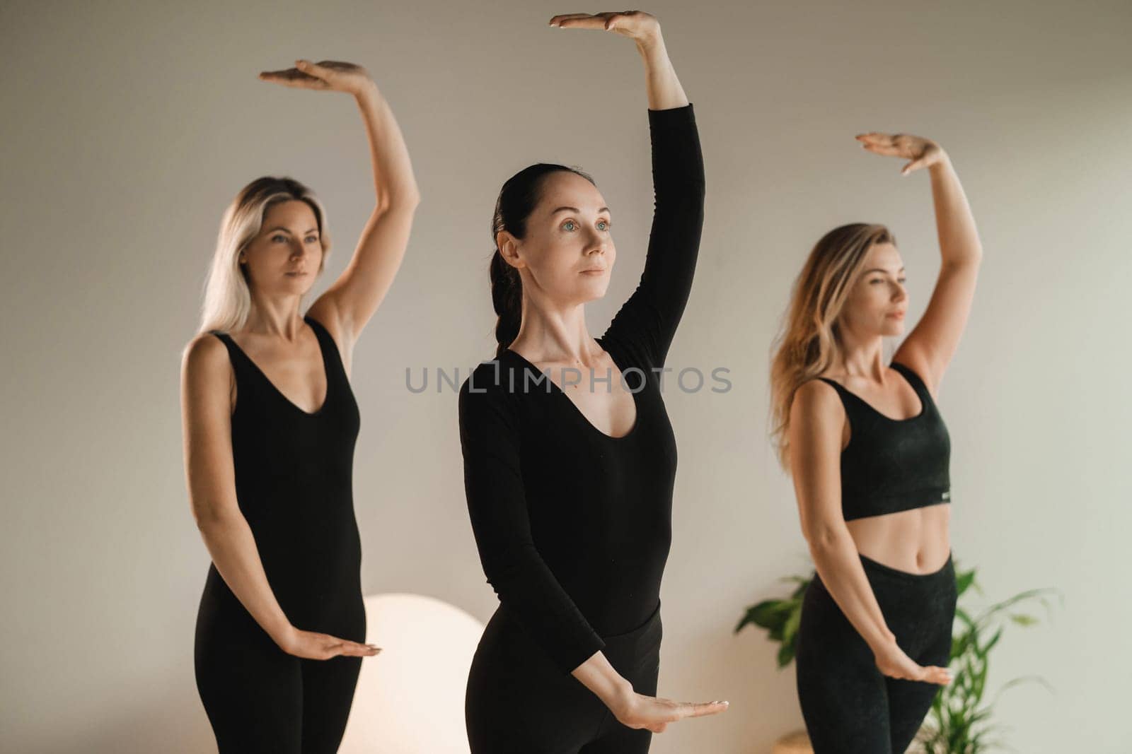 A group of girls in black doing yoga poses indoors. Women are engaged in fitness by Lobachad