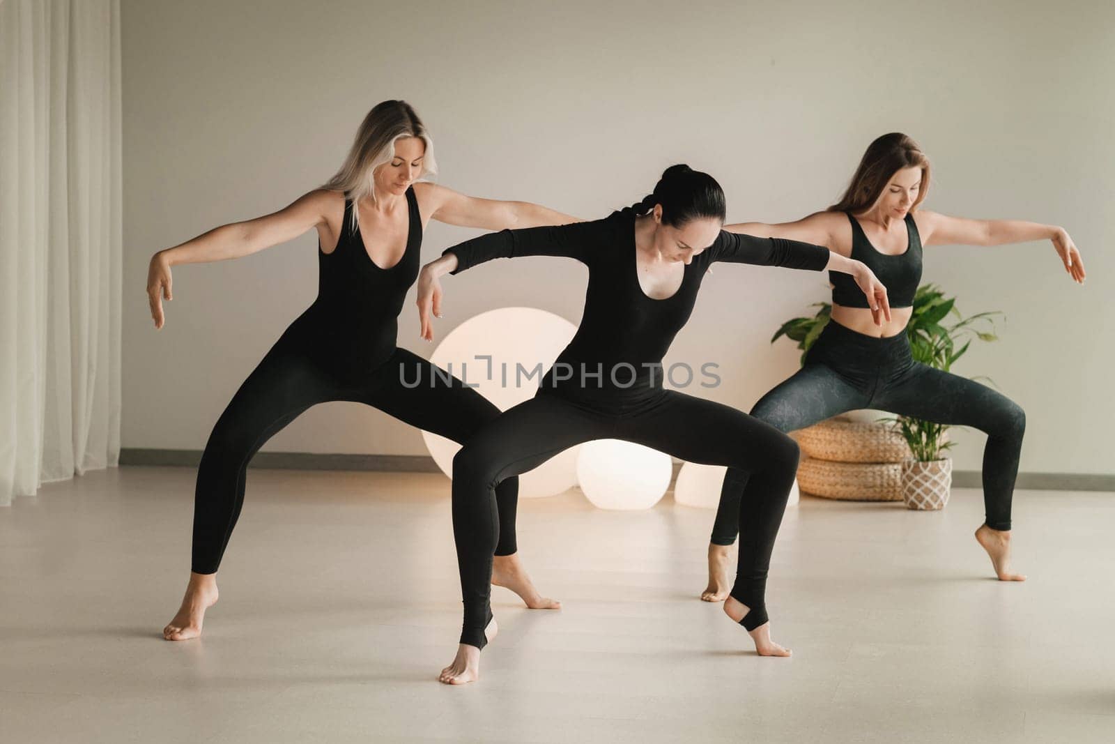 A group of girls in black doing yoga poses indoors. Women are engaged in fitness.