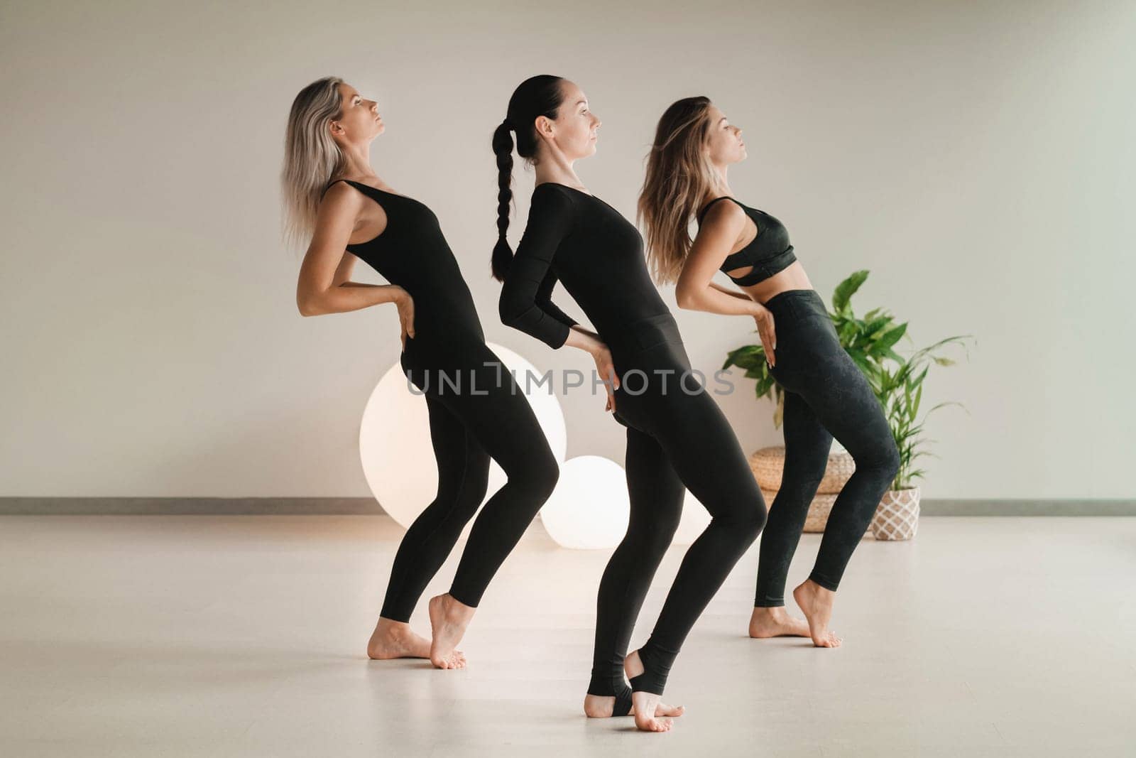 A group of girls in black doing yoga poses indoors. Women are engaged in fitness by Lobachad