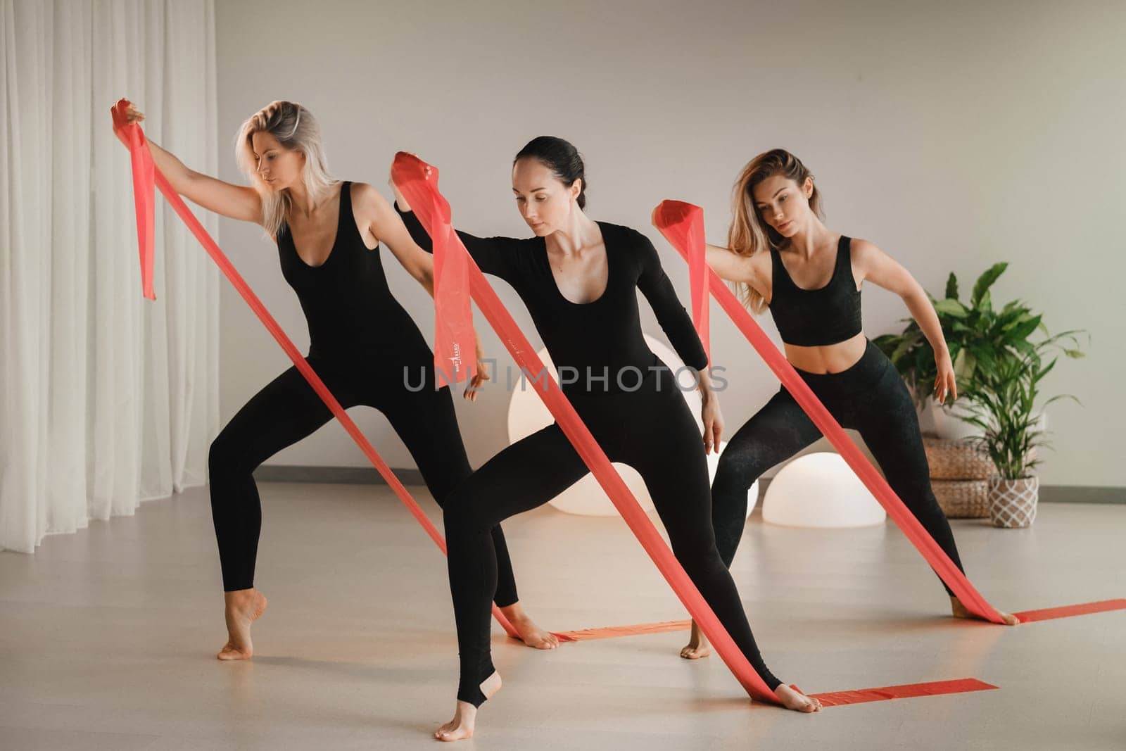 Girls in black are doing fitness with red ribbons indoors.
