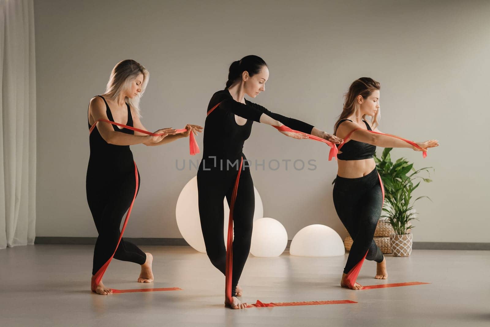 Girls in black are doing fitness with red ribbons indoors.