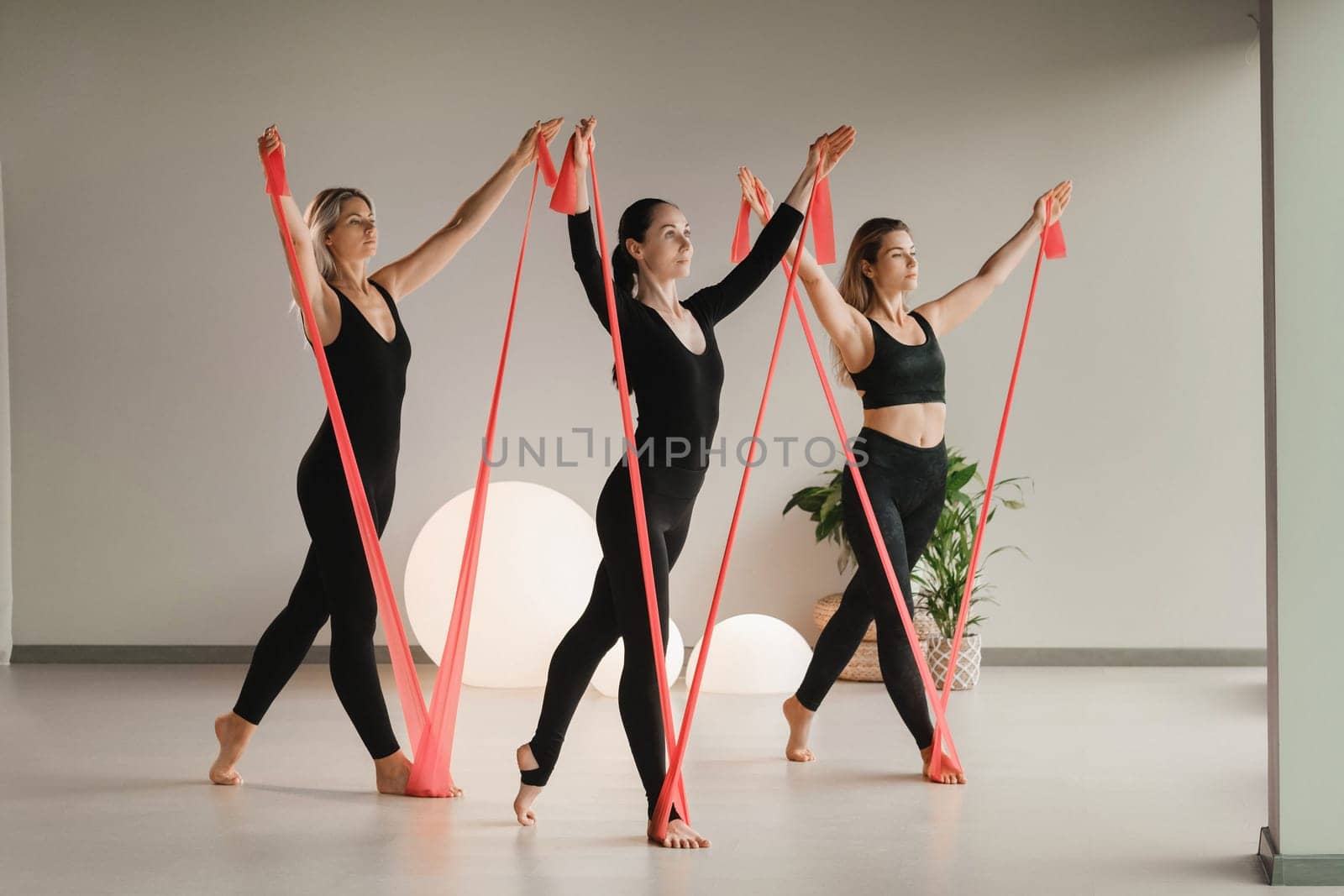 Girls in black are doing fitness with red ribbons indoors by Lobachad