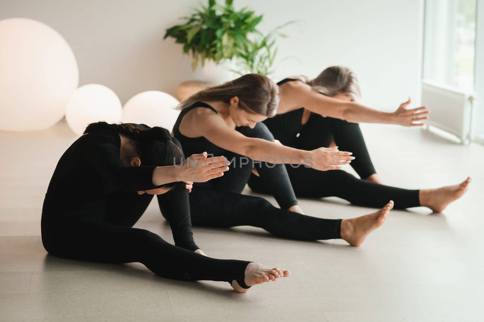 A group of girls in black doing yoga poses indoors. Women are engaged in fitness by Lobachad