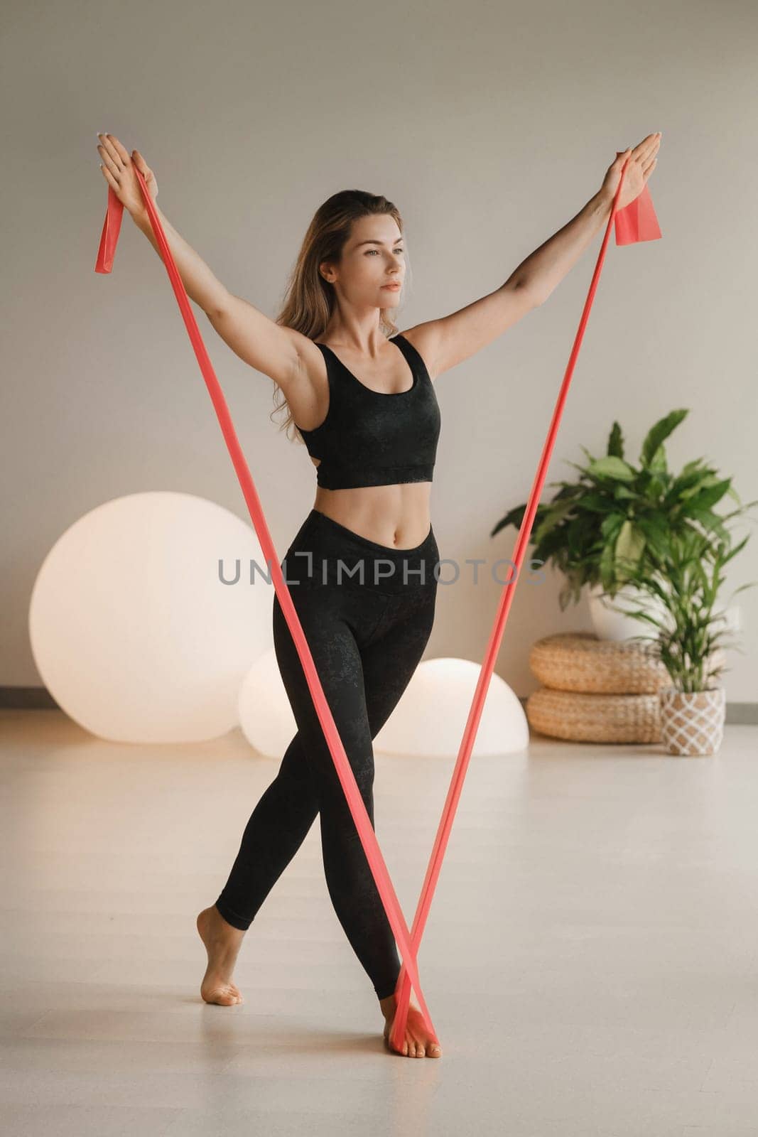 Girl in black doing fitness with red ribbons indoors.