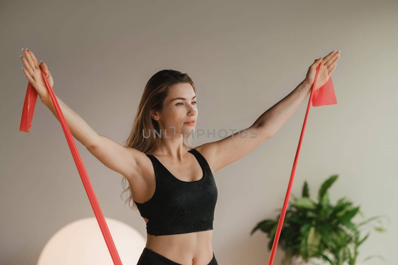 Girl in black doing fitness with red ribbons indoors.