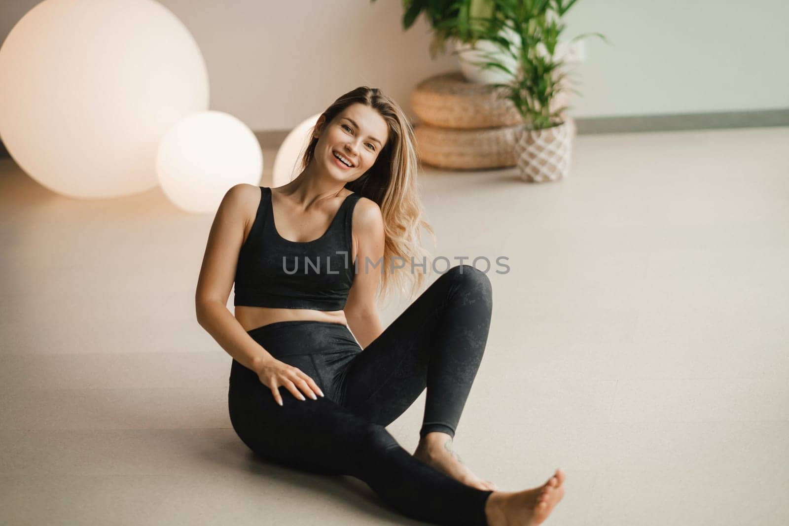 Portrait of a girl in black clothes sitting on the floor before doing yoga indoors by Lobachad
