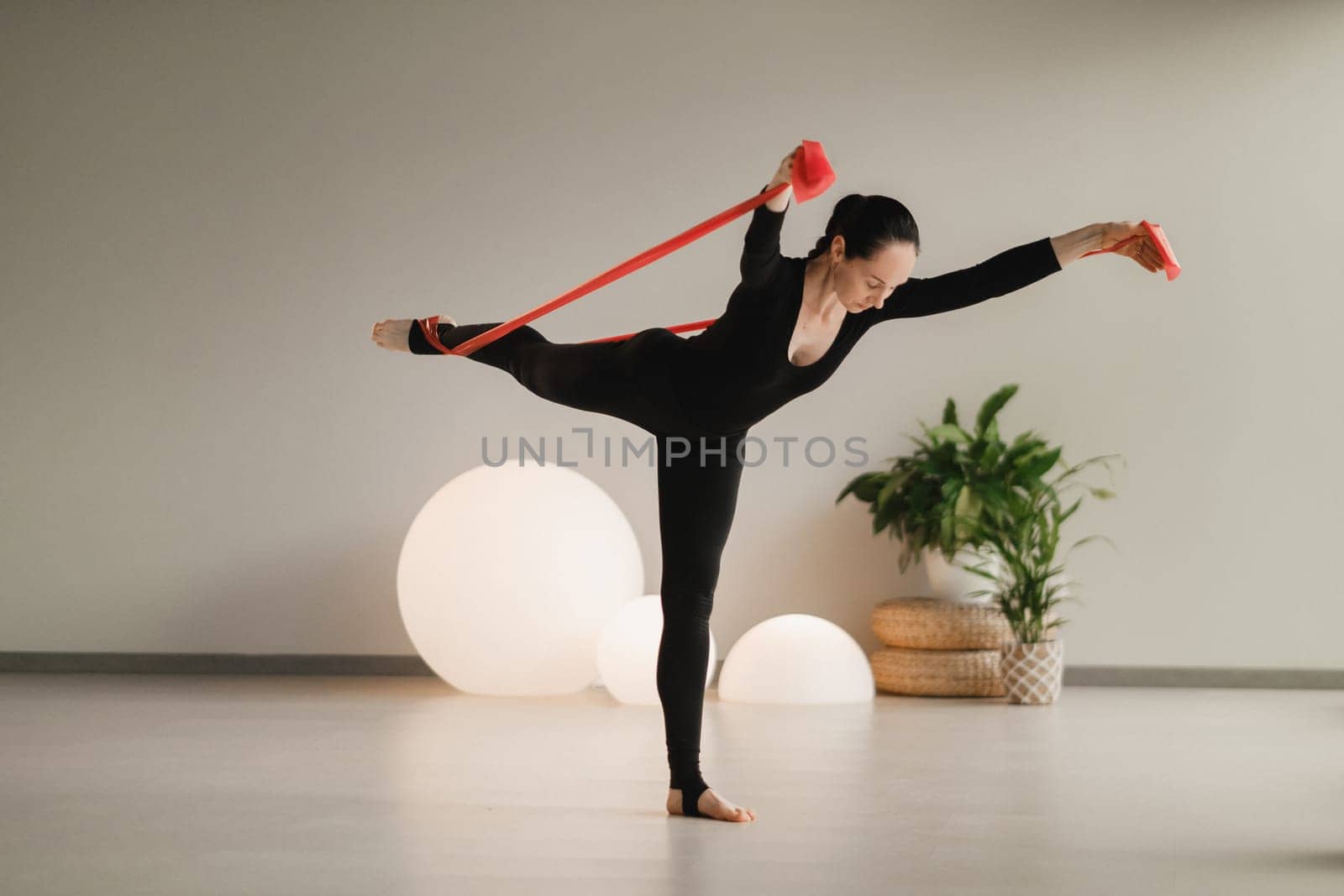 Girl in black doing fitness with red ribbons indoors by Lobachad