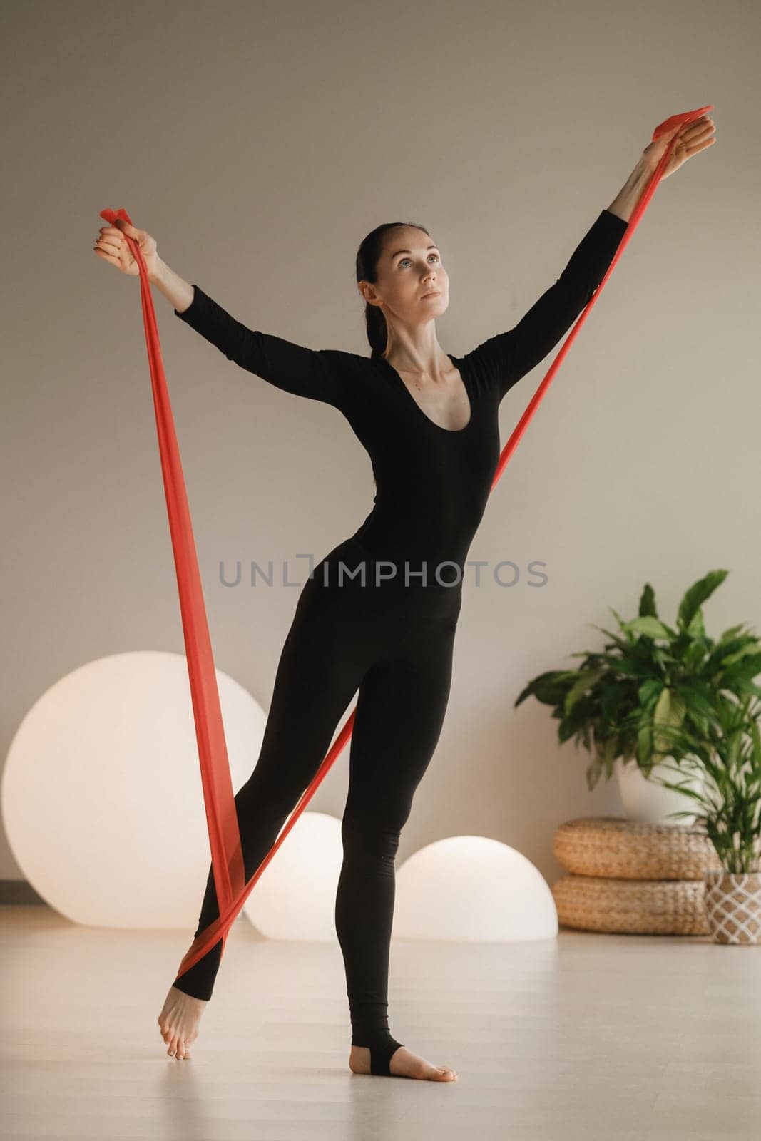 Girl in black doing fitness with red ribbons indoors.