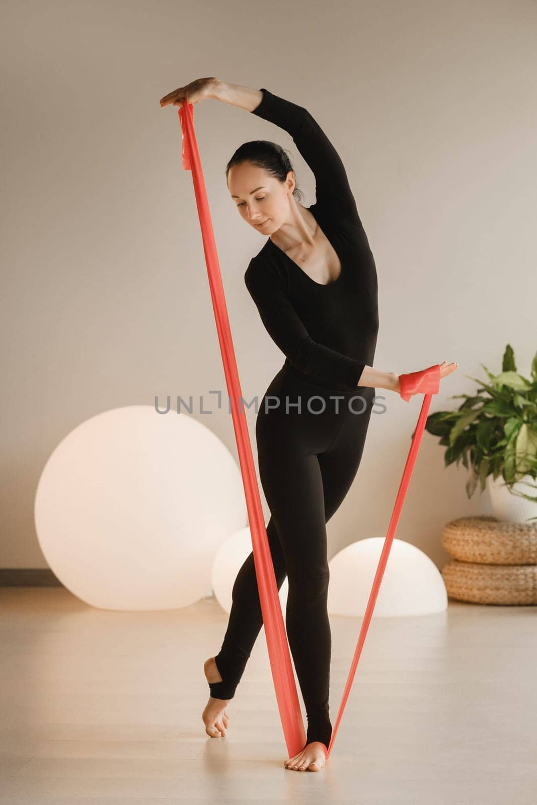 Girl in black doing fitness with red ribbons indoors.