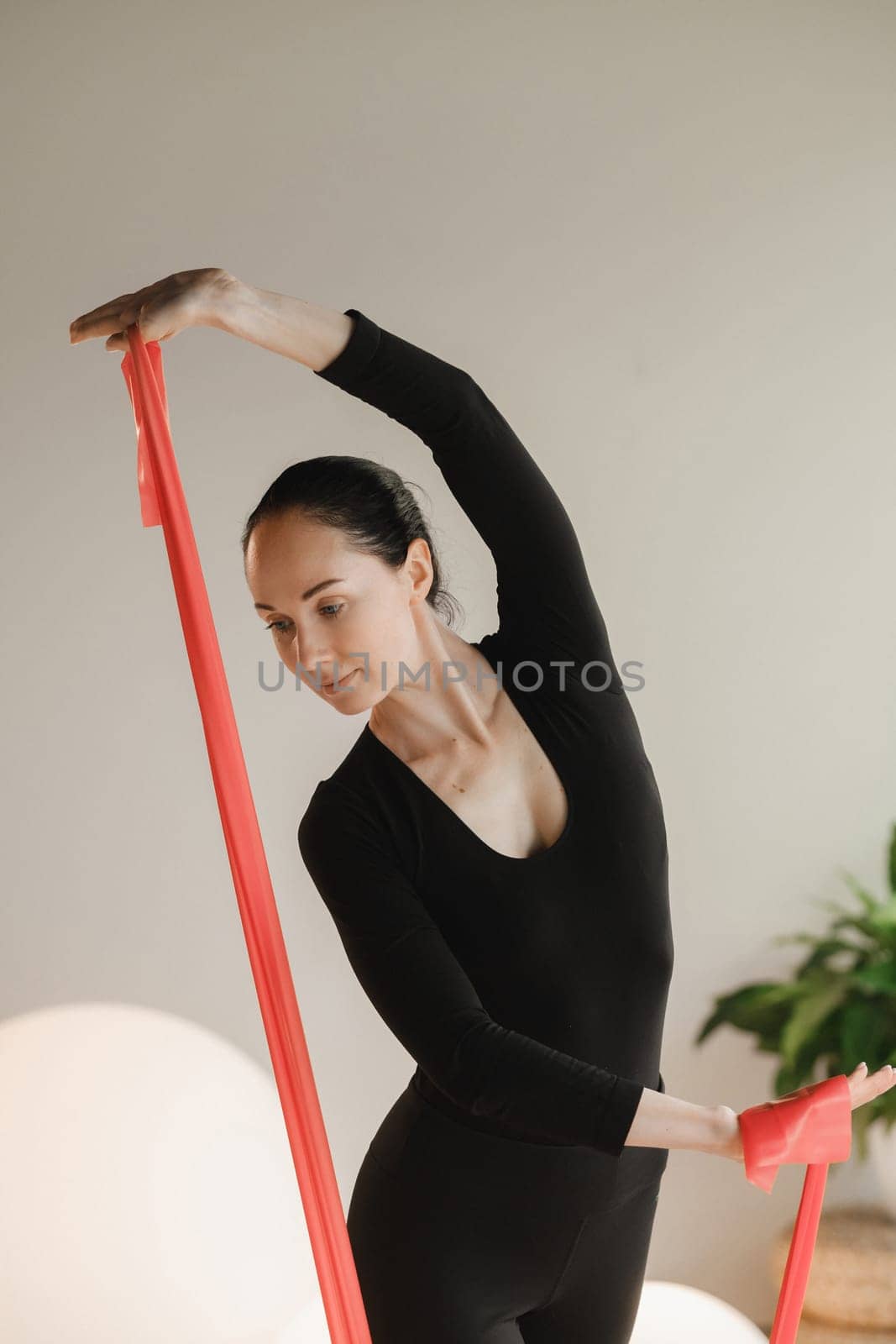 Girl in black doing fitness with red ribbons indoors.