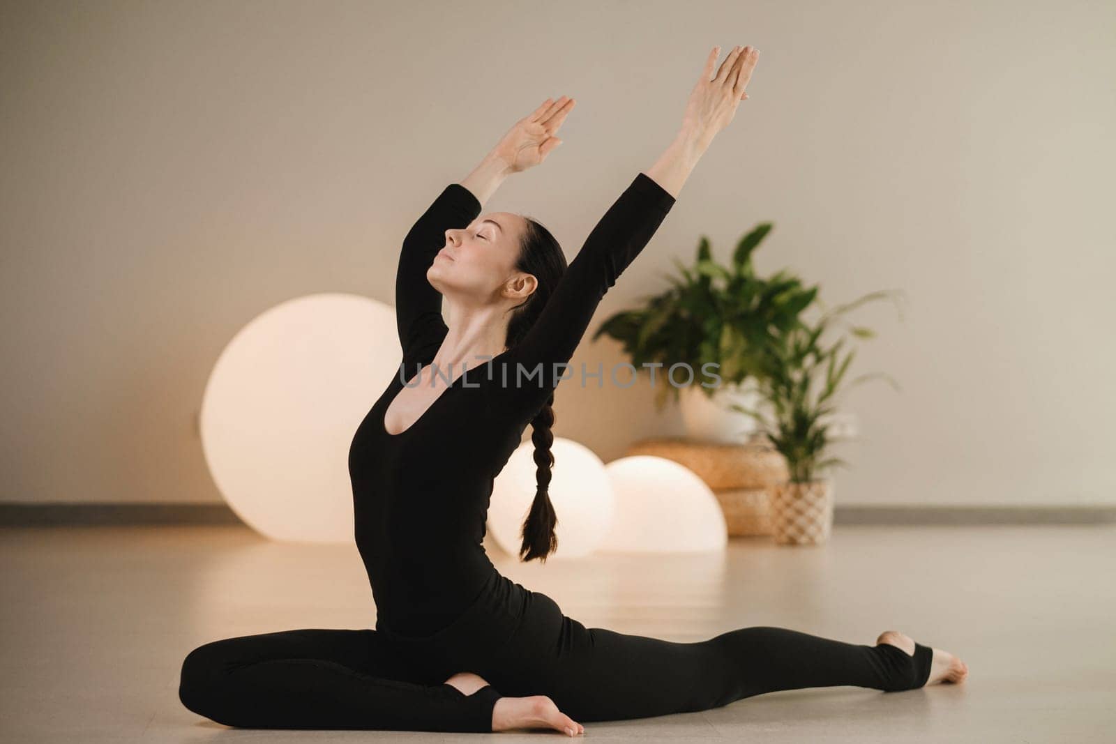 A girl in black clothes does yoga on a mat indoors by Lobachad