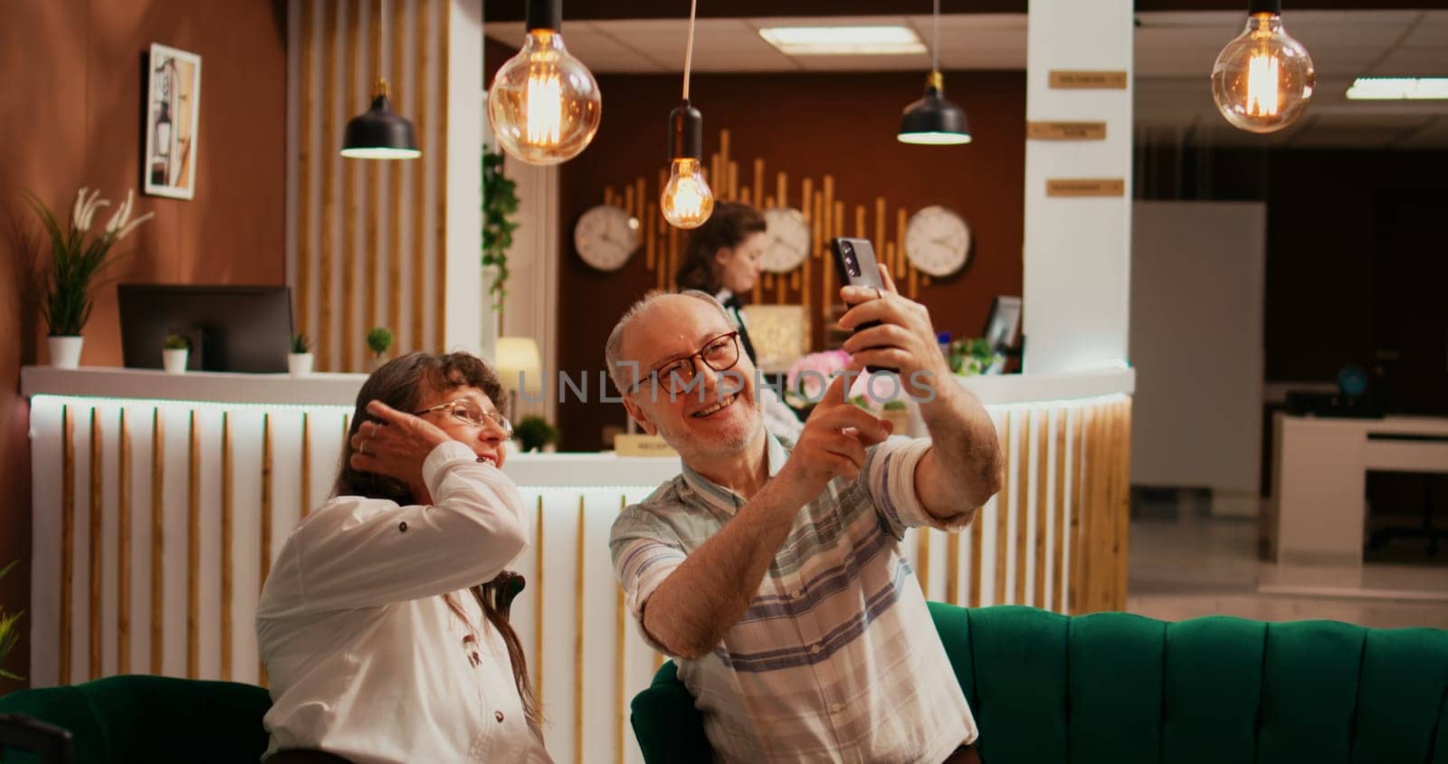 Elderly people taking photos in lobby, recording all activities on retirement vacation abroad. Old husband and wife take pictures on smartphone, making memories for family members.