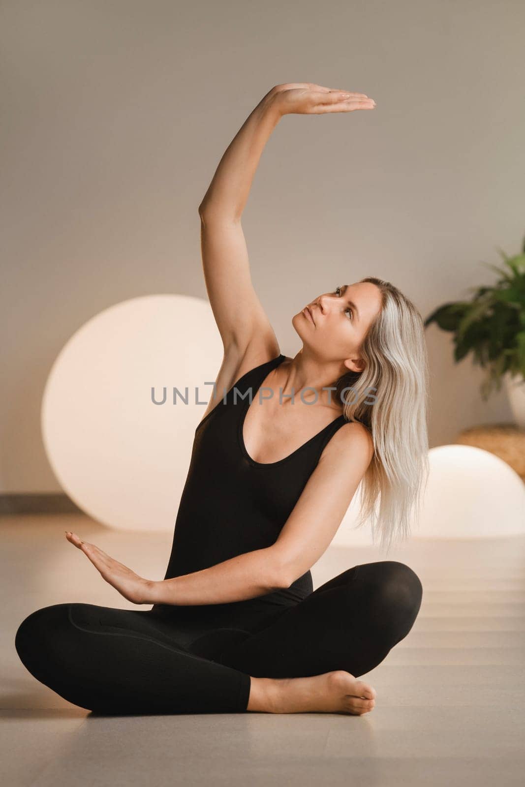 A girl in black clothes does yoga on a mat indoors.