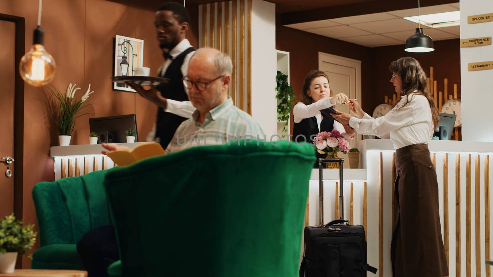 Old woman filling in registration forms at front desk, passing room check in and preparing to start retirement vacation trip. Traveller asking receptionist about all inclusive service. Handheld shot.