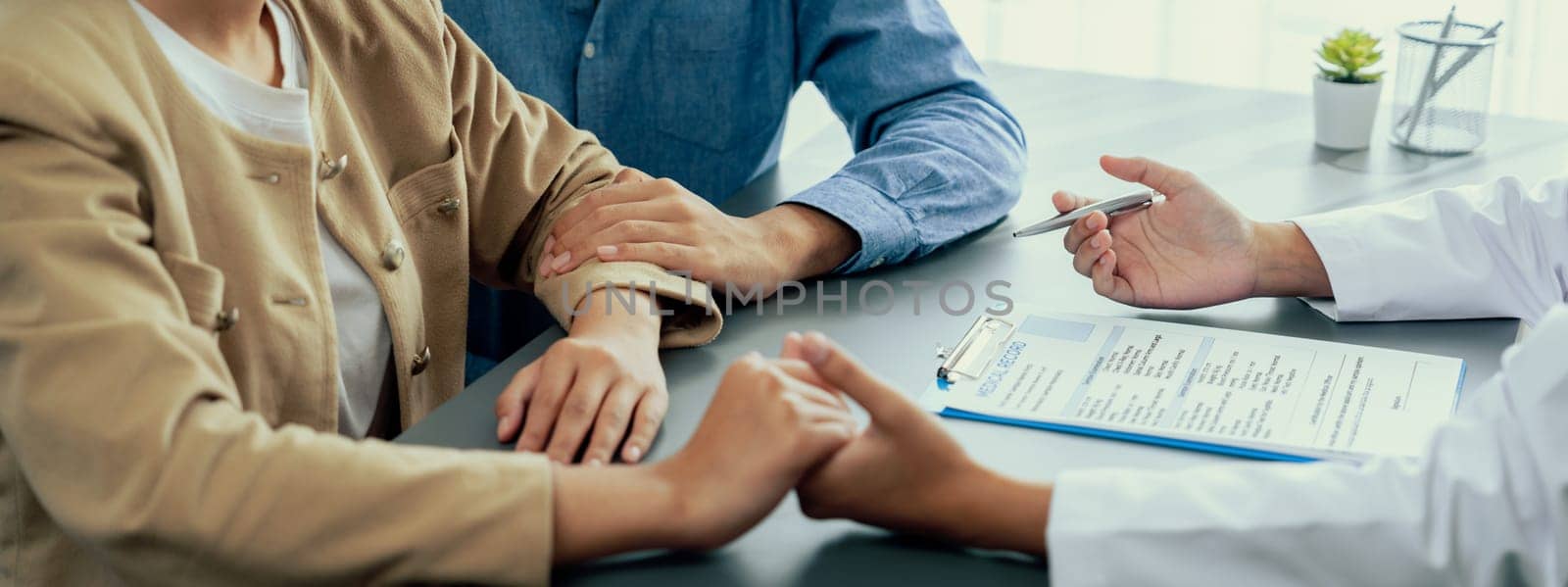 Doctor providing compassionate healthcare consultation while young couple patient holding hand, comfort each other after infertile report. Reproductive and medical fertility consulting. Neoteric