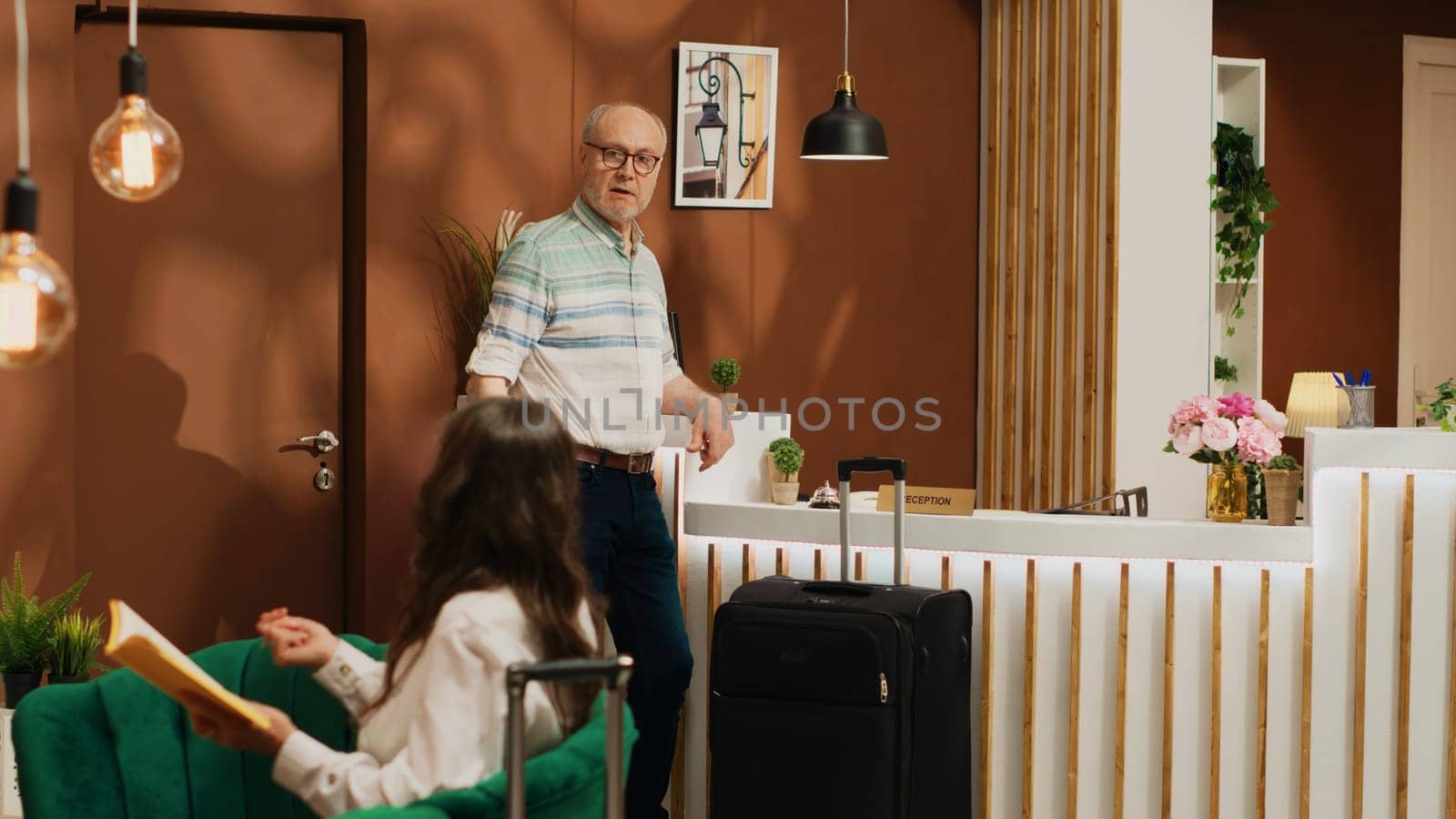 Retired man ringing service bell to do check in at hotel reception, arriving at luxury resort on holiday. Person at retirement age travelling on vacation abroad, front desk employees. Tripod shot.