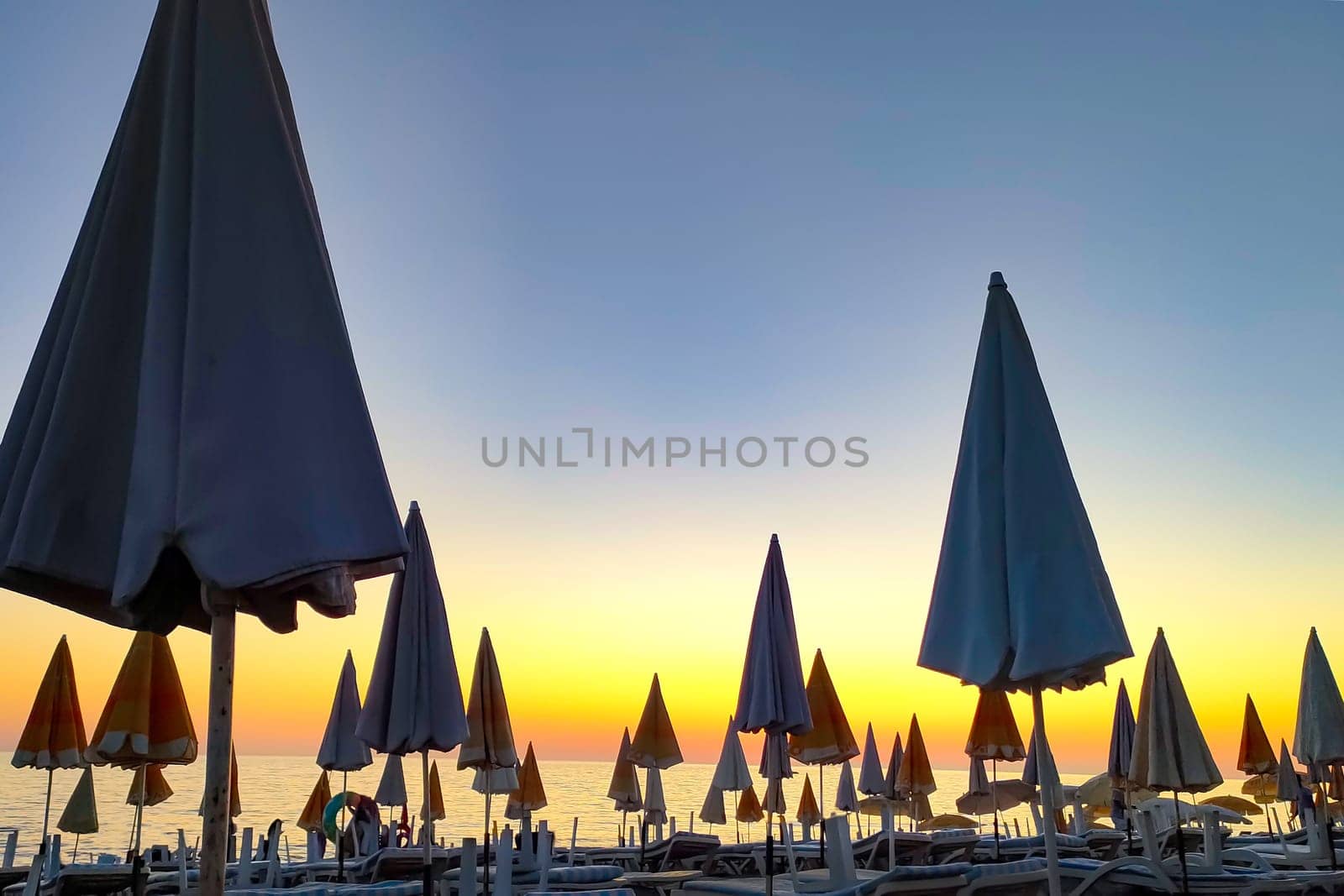 Closed beach umbrellas against background of sunset evening sky, concept of vacation and closing of season. by Laguna781