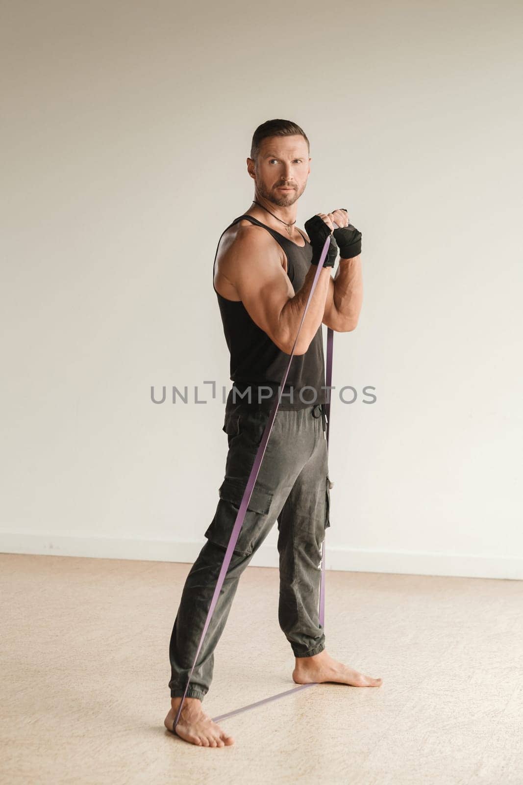 A man in black sportswear is engaged in strength fitness using a rubber loop indoors.