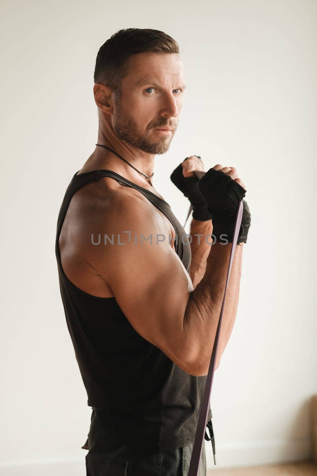 A man in black sportswear is engaged in strength fitness using a rubber loop indoors.