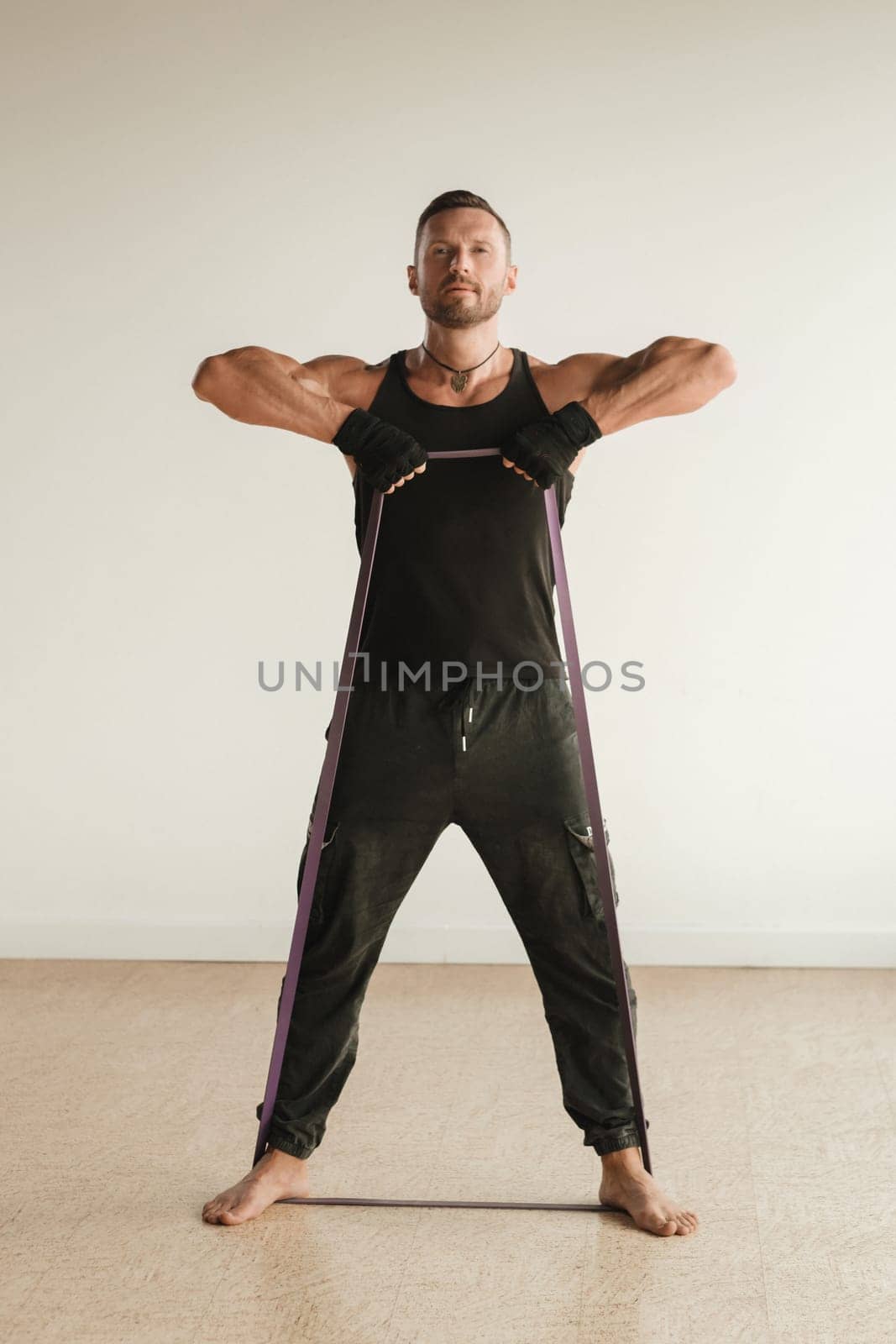 A man in black sportswear is engaged in strength fitness using a rubber loop indoors.