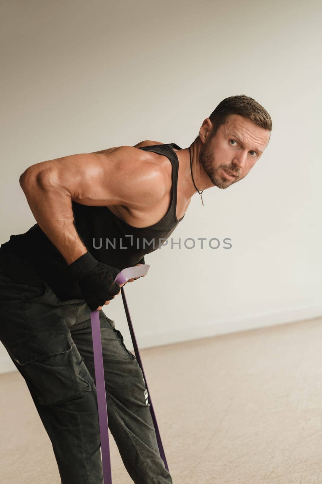 A man in black sportswear is engaged in strength fitness using a rubber loop indoors by Lobachad