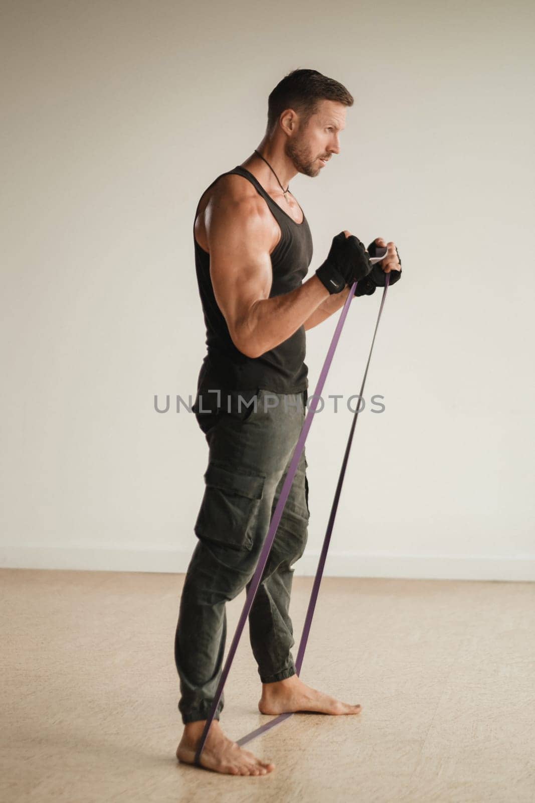 A man in black sportswear is engaged in strength fitness using a rubber loop indoors by Lobachad