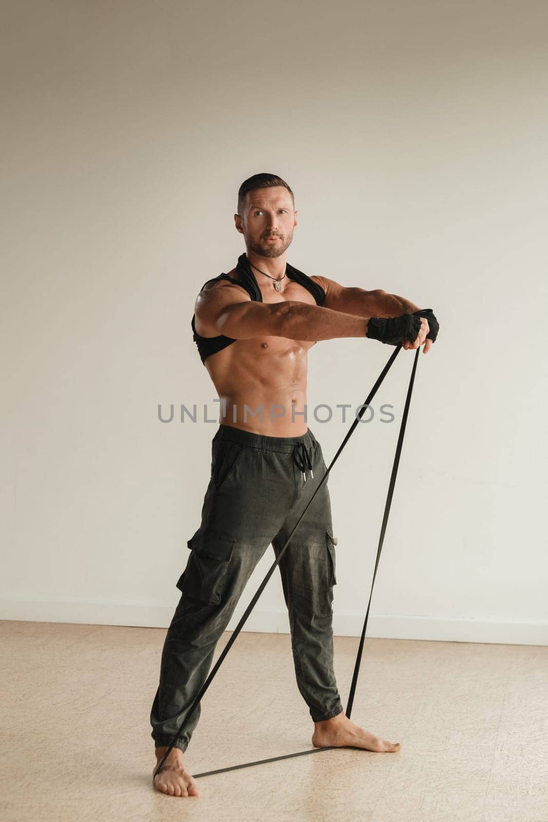 A man with a naked torso is engaged in strength fitness using a rubber loop indoors.