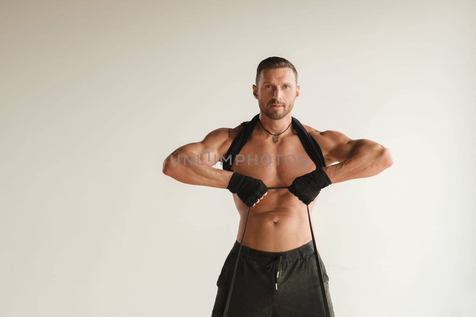 A man with a naked torso is engaged in strength fitness using a rubber loop indoors.