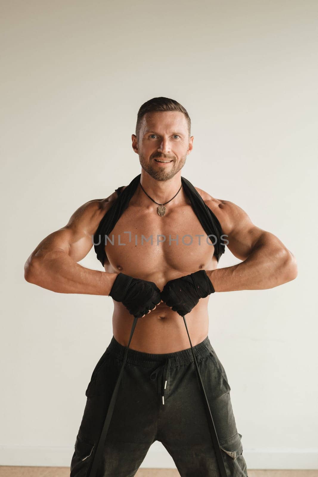 A man with a naked torso is engaged in strength fitness using a rubber loop indoors.