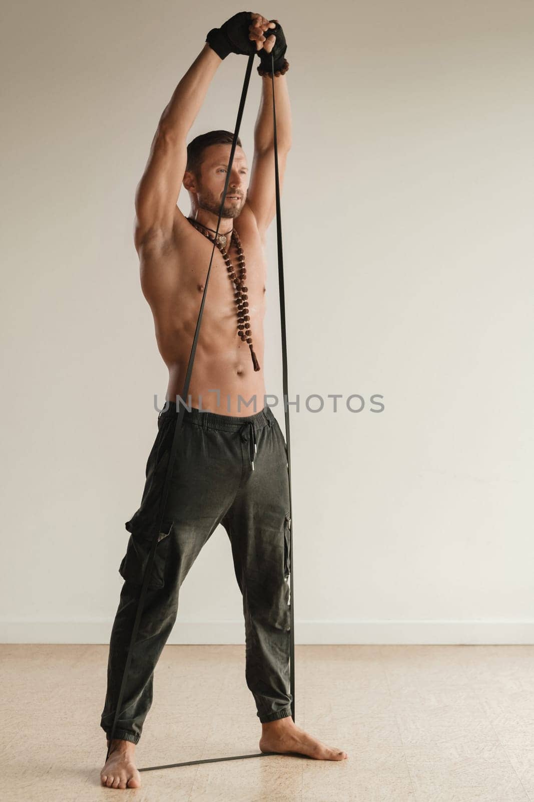 A man with a naked torso is engaged in strength fitness using a rubber loop indoors by Lobachad