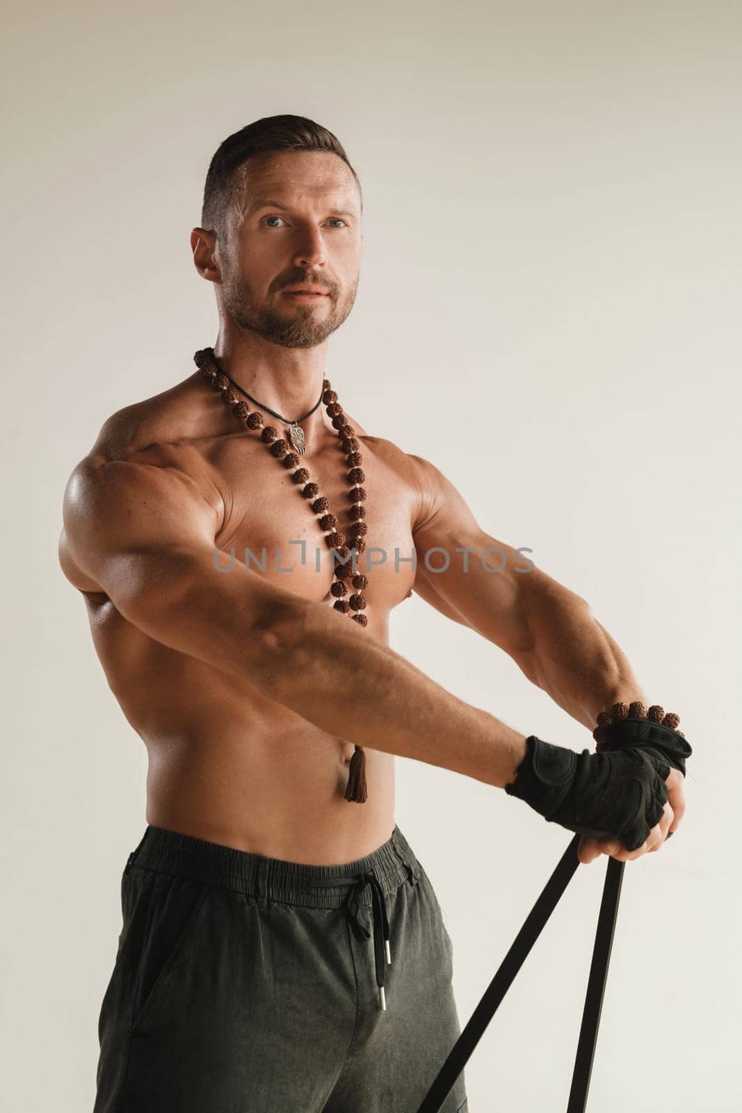 A man with a naked torso is engaged in strength fitness using a rubber loop indoors by Lobachad
