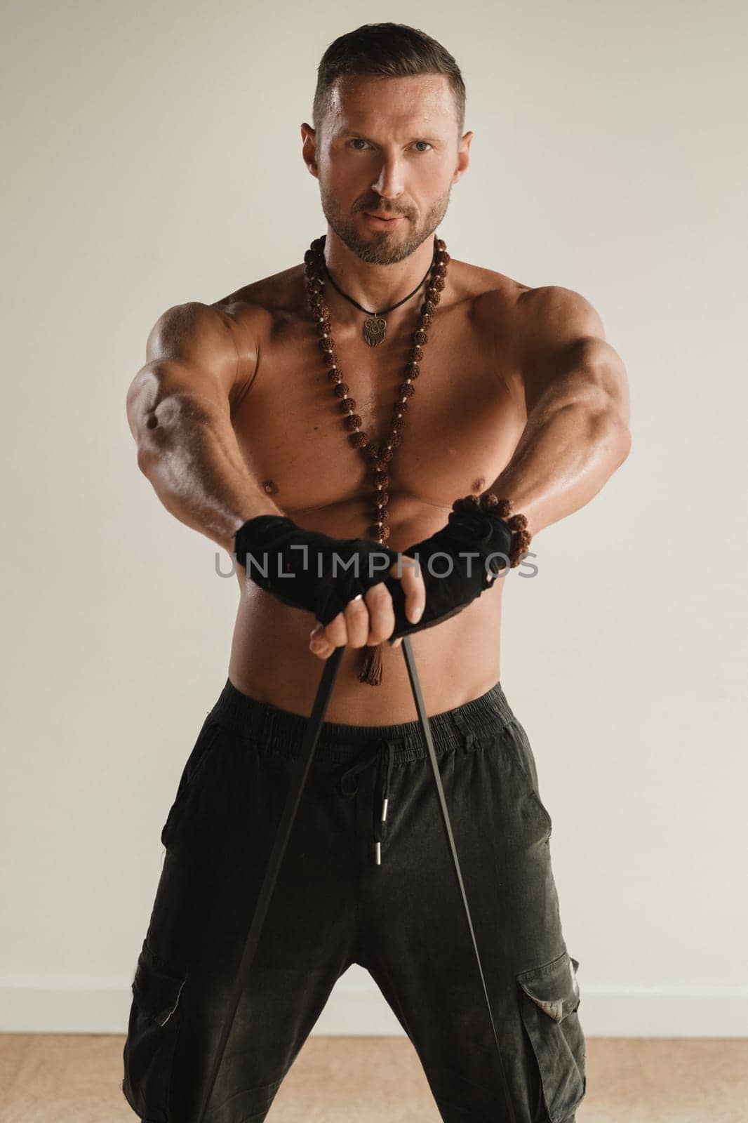 A man with a naked torso is engaged in strength fitness using a rubber loop indoors by Lobachad