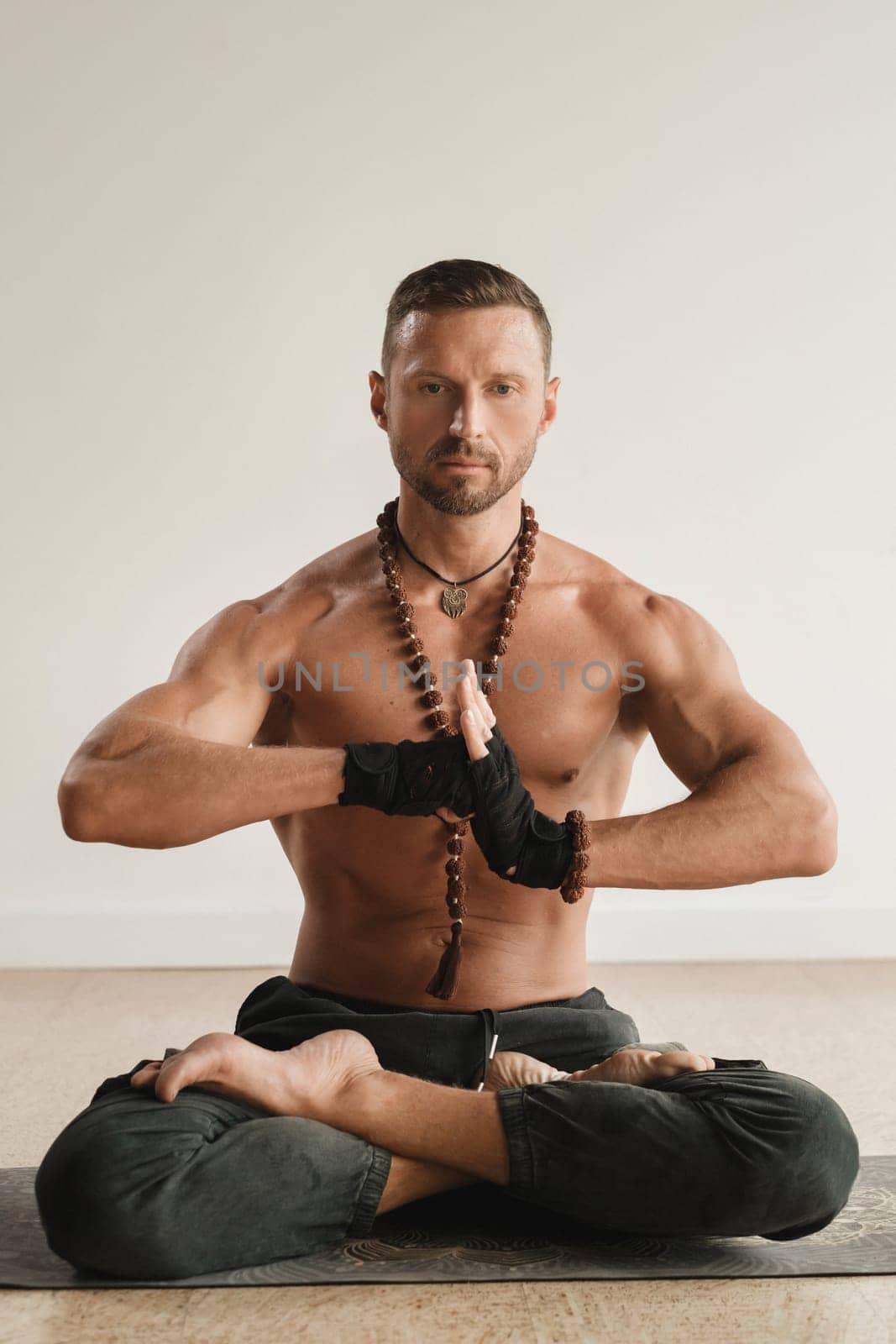 a man with a naked torso is sitting in the lotus position before doing yoga indoors. Fitness Trainer.