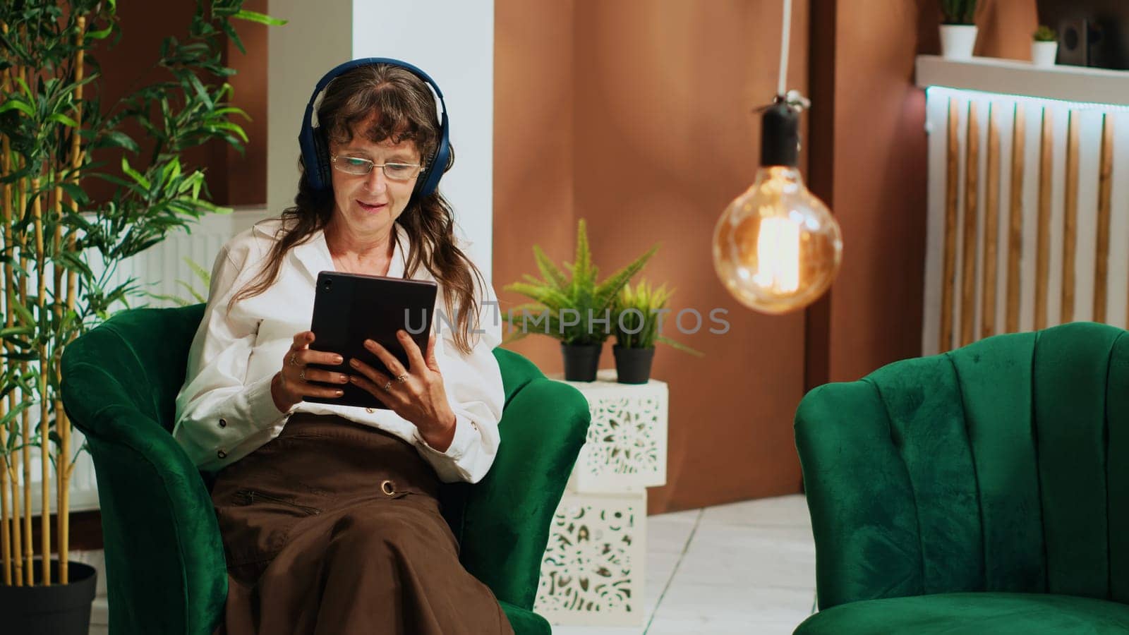 Elderly woman using gadget on couch, watches film on online streaming services while she waits to see room. Older tourist enjoying modern technology on tablet at all inclusive hotel.