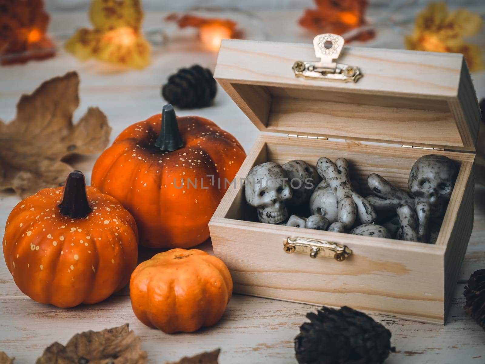 A chest with skulls and bones, three pumpkins, leaves, cones, a garland lie on a wooden table, side view close-up. Happy halloween concept.