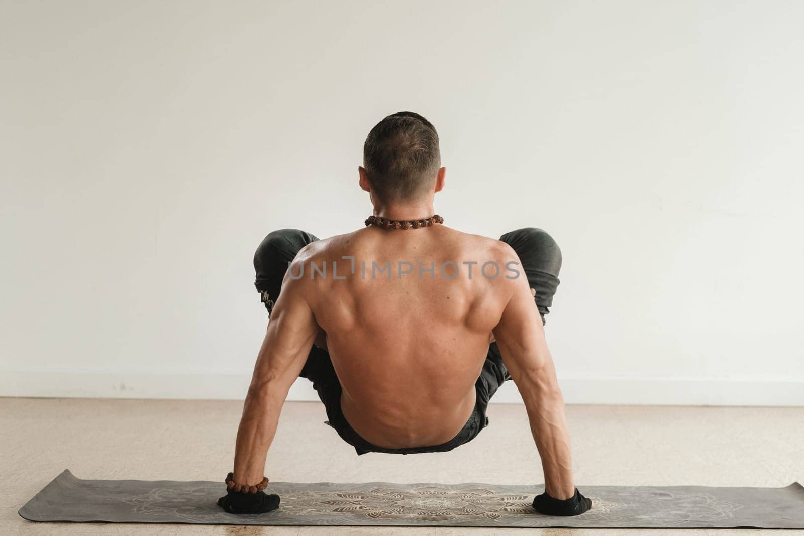 a man with a naked torso does yoga standing on his hands indoors. Fitness Trainer.