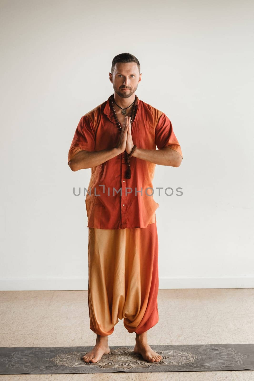 a man in an orange suit does yoga in a fitness room. The concept of health by Lobachad