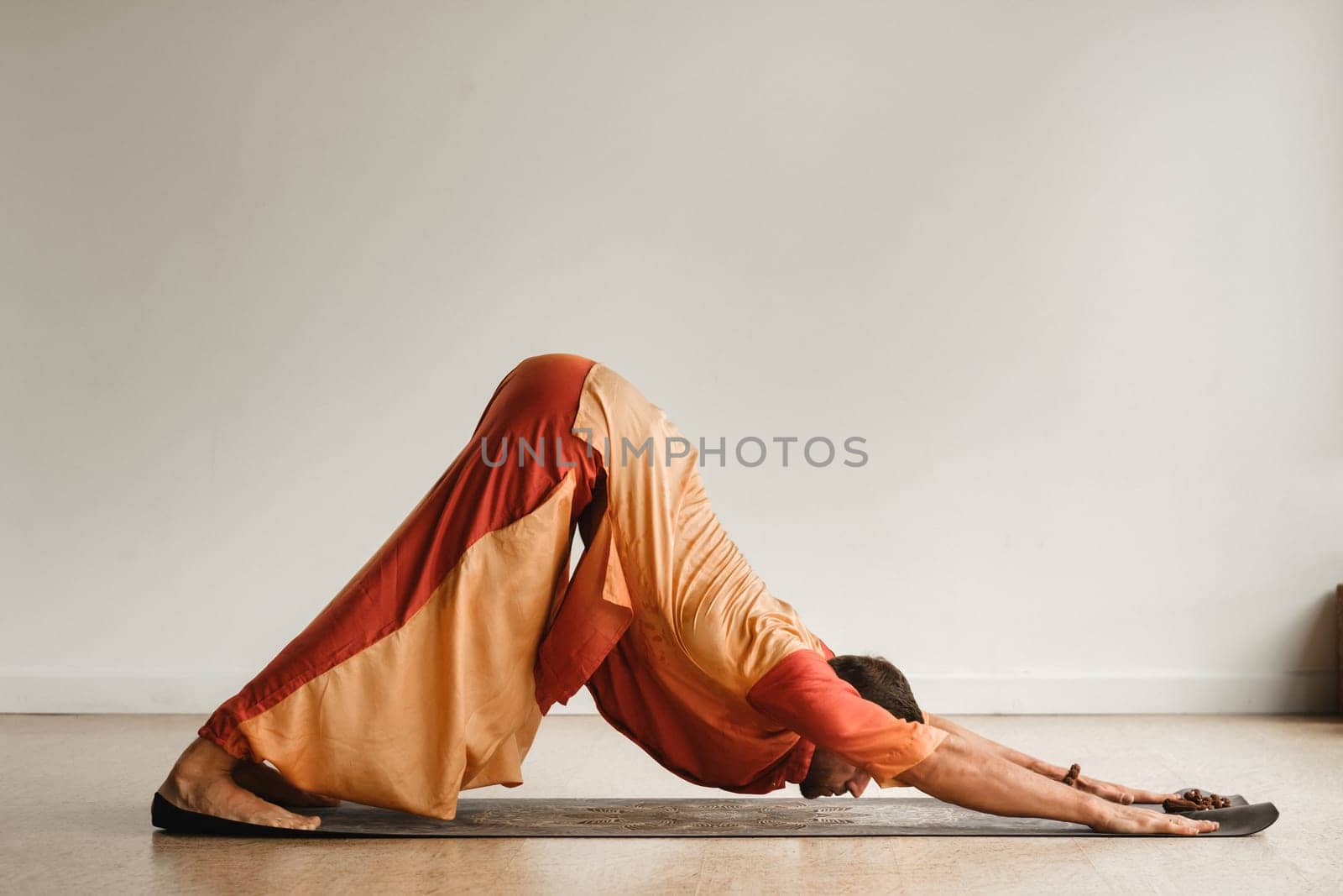 a man in an orange suit does yoga in a fitness room. The concept of health by Lobachad