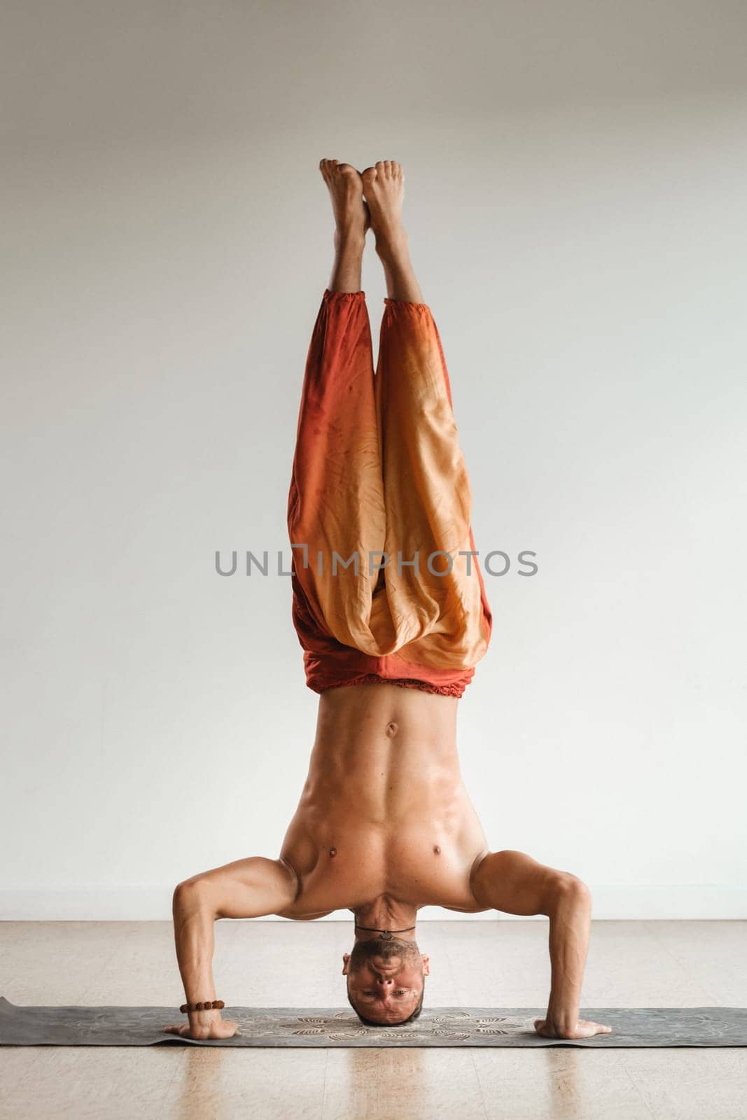 a man with a naked torso does yoga standing on his head indoors. Fitness Trainer.