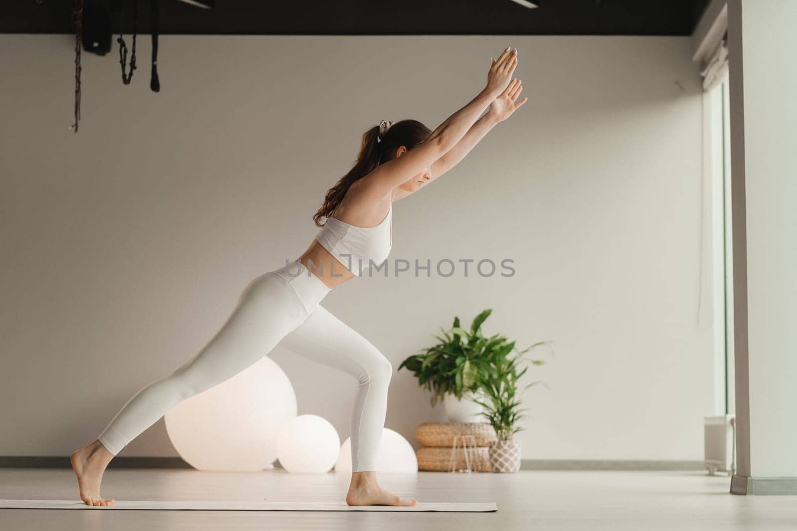 A girl in white clothes does yoga on a mat indoors.