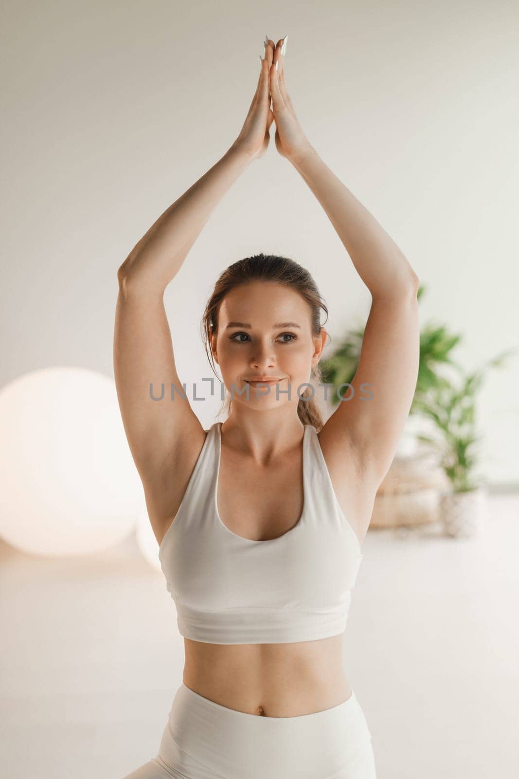 A girl in white clothes does yoga on a mat indoors.