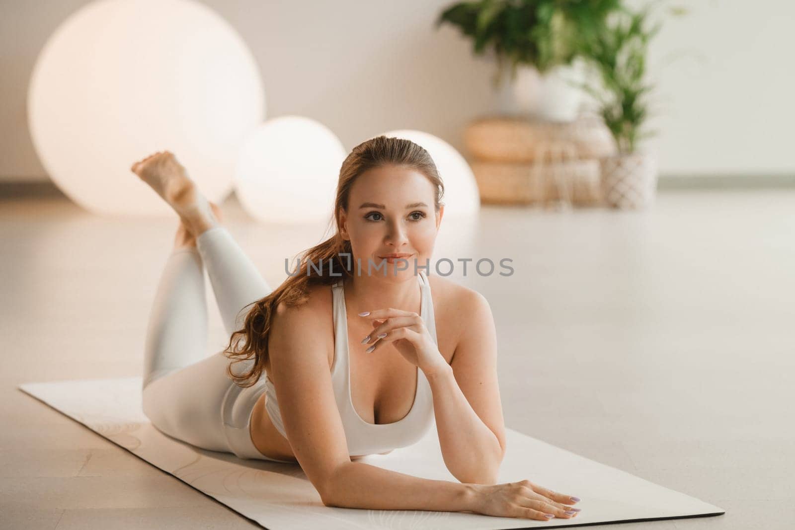 Portrait of a girl in white clothes lying on a mat before doing yoga indoors.