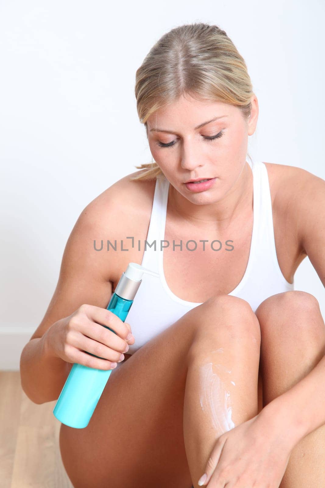 Beautiful blond woman moisturizing her legs