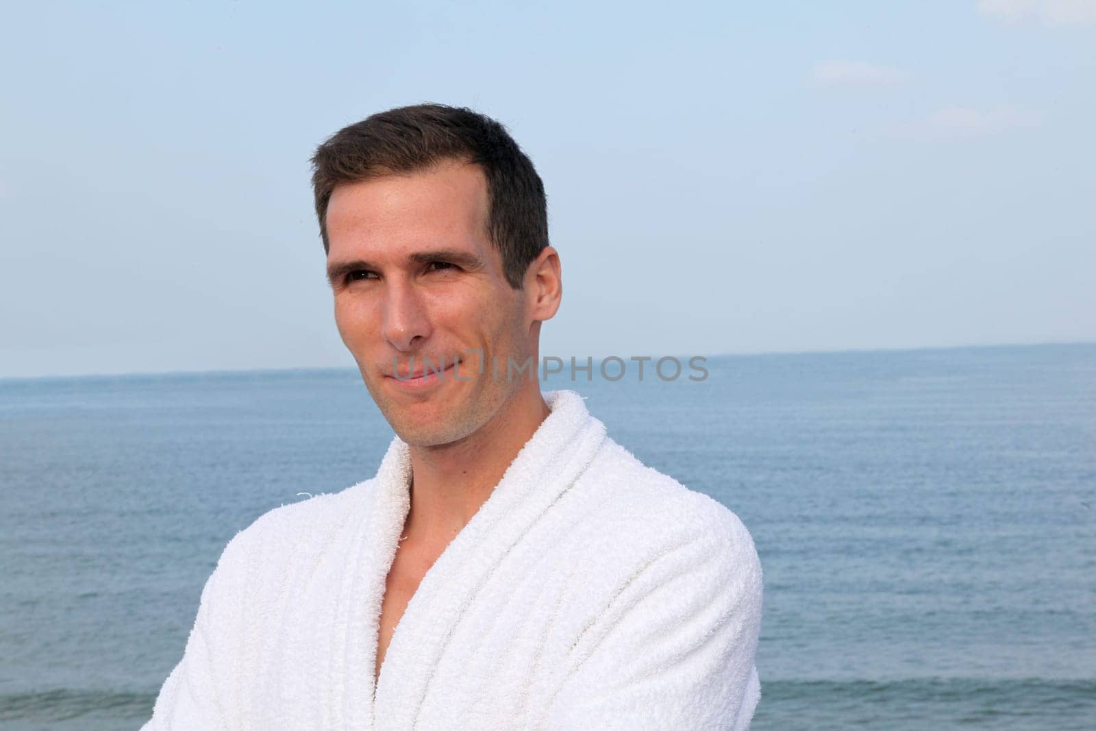 Smiling man standing by the sea in bathrobe
