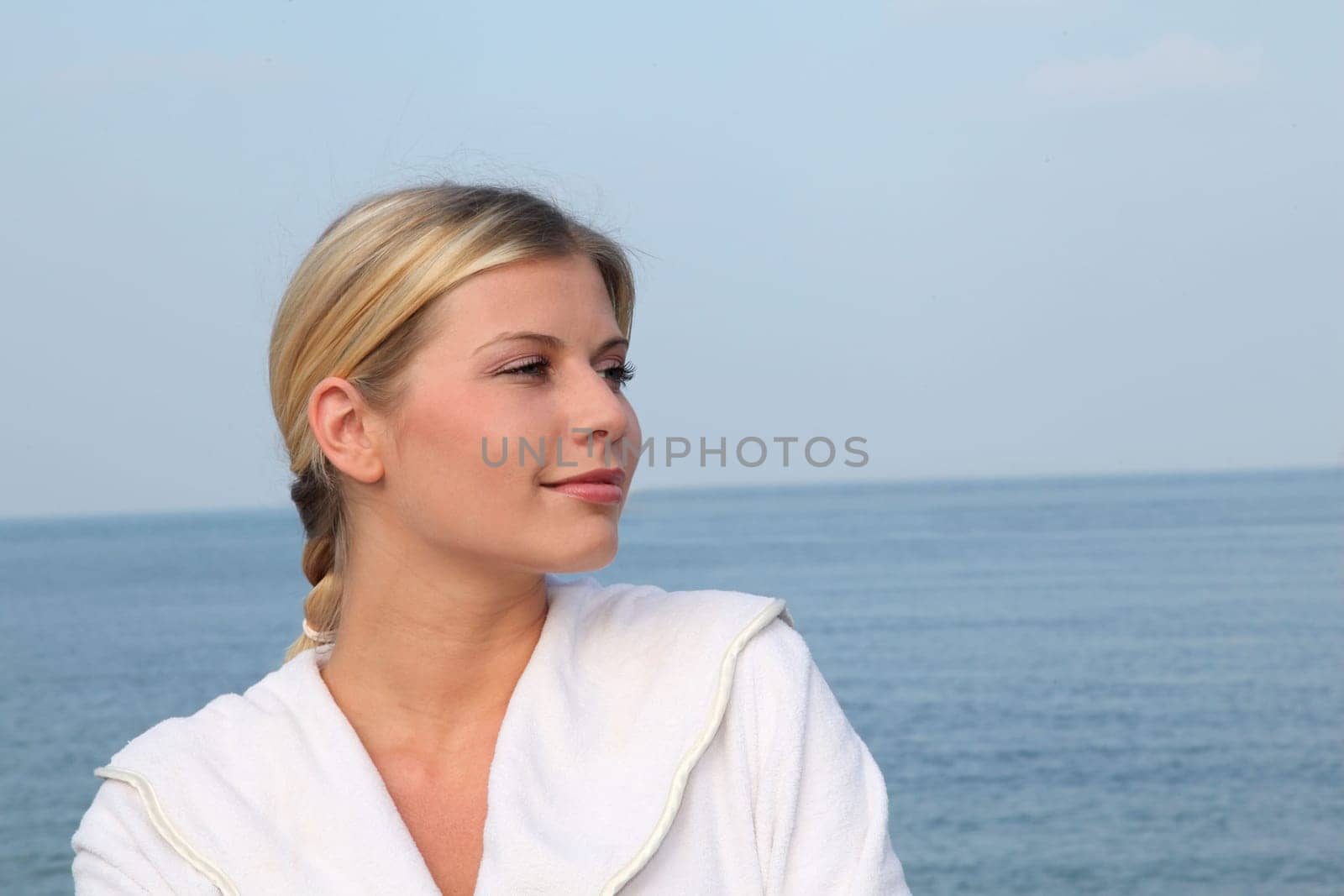 Smiling beautiful woman standing by the sea in bathrobe