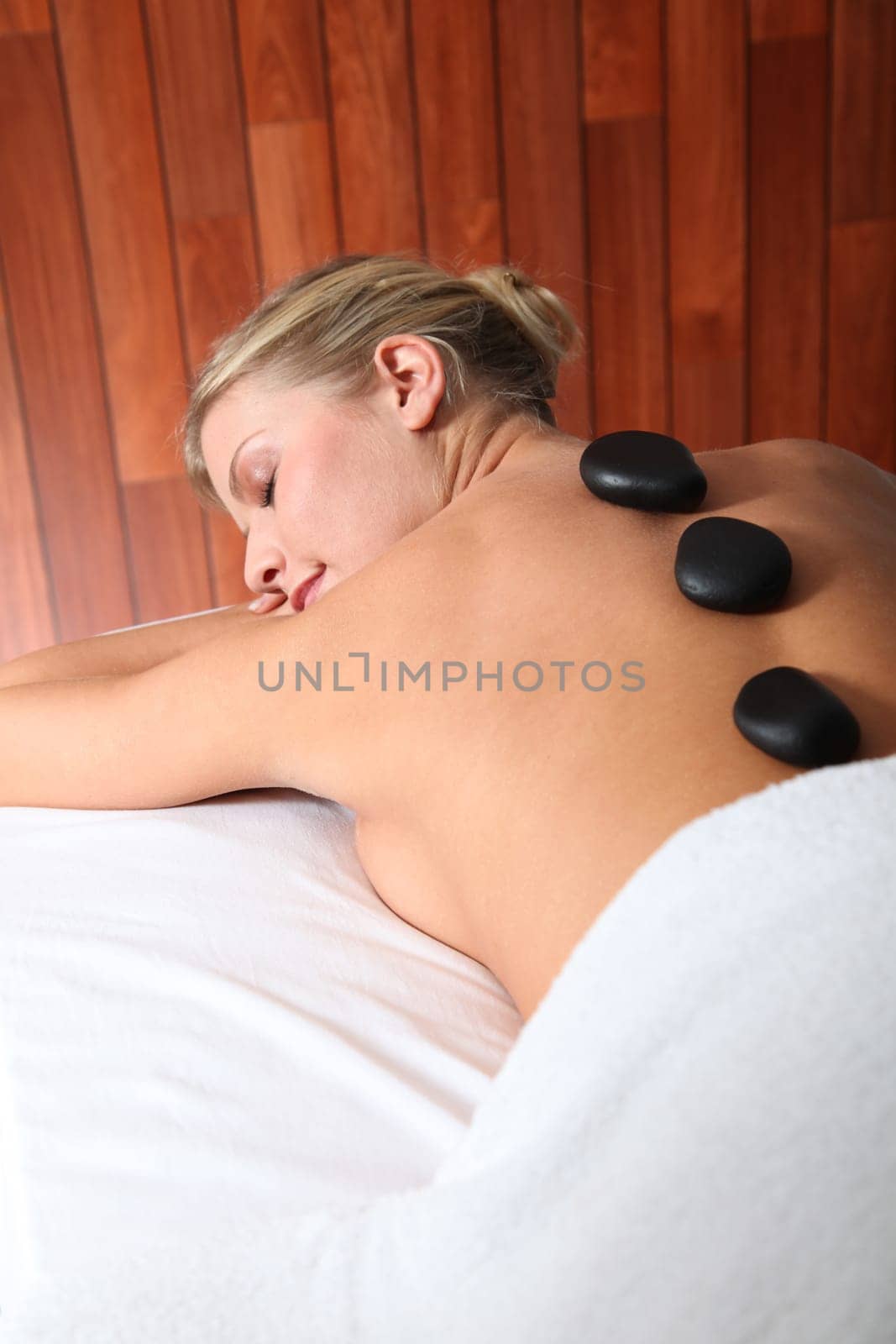 Blond woman laying on massage bed with hot stones