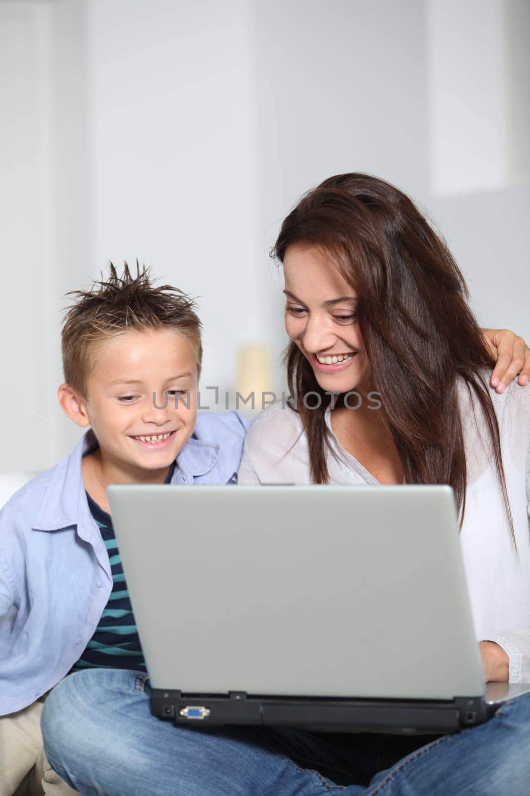 Little boy and mother sitting on sofa at home with laptop