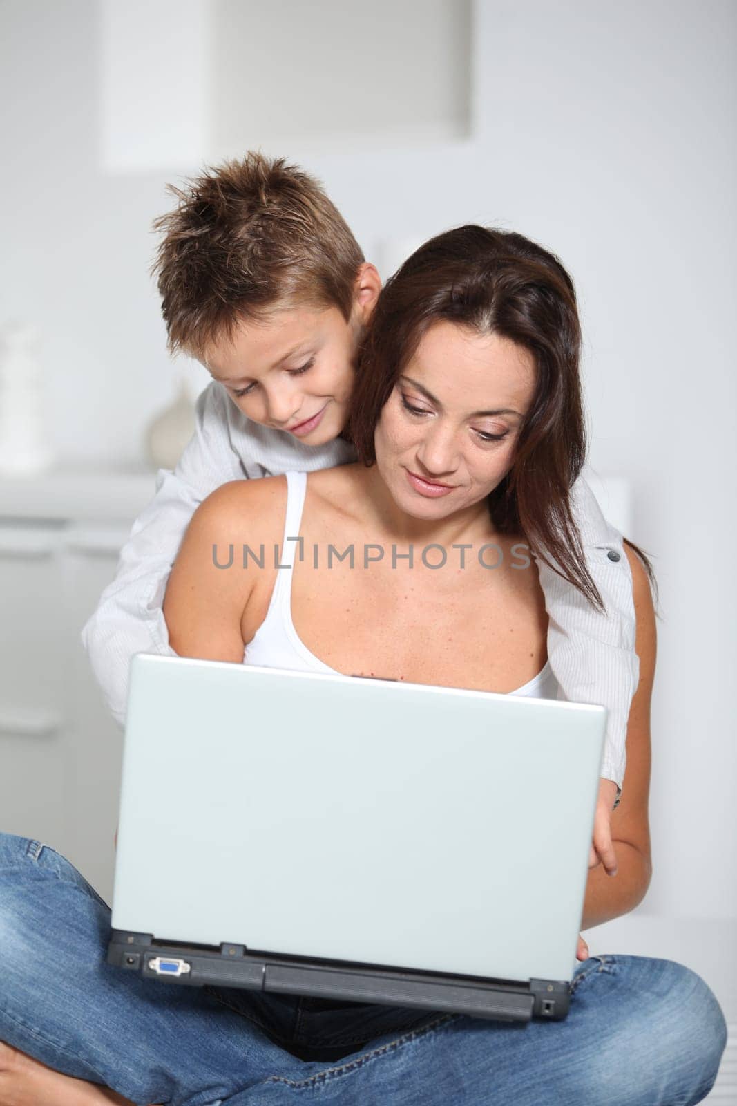 Little boy and mother sitting on sofa at home with laptop
