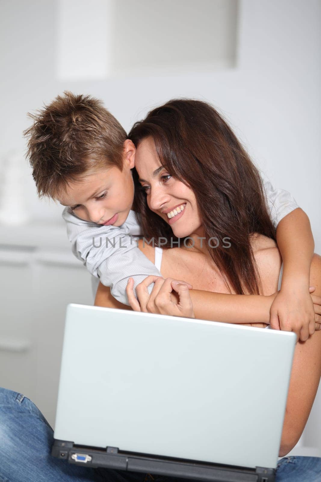 Little boy and mother sitting on sofa at home with laptop